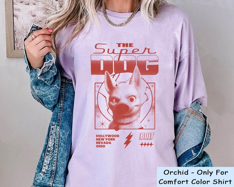 May include: Orchid-colored t-shirt with a red graphic of a dog and the text "THE SUPER DOG." Additional text includes "HOLLYWOOD NEW YORK NEVADA OHIO" and "BOLT." The shirt is a Comfort Color brand.