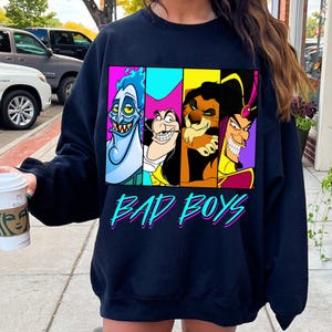 May include: Navy blue sweatshirt featuring four cartoon villains in colorful panels. The characters include Hades, Captain Hook, Scar, and Jafar. The words "BAD BOYS" are written in a teal and pink font below the characters.