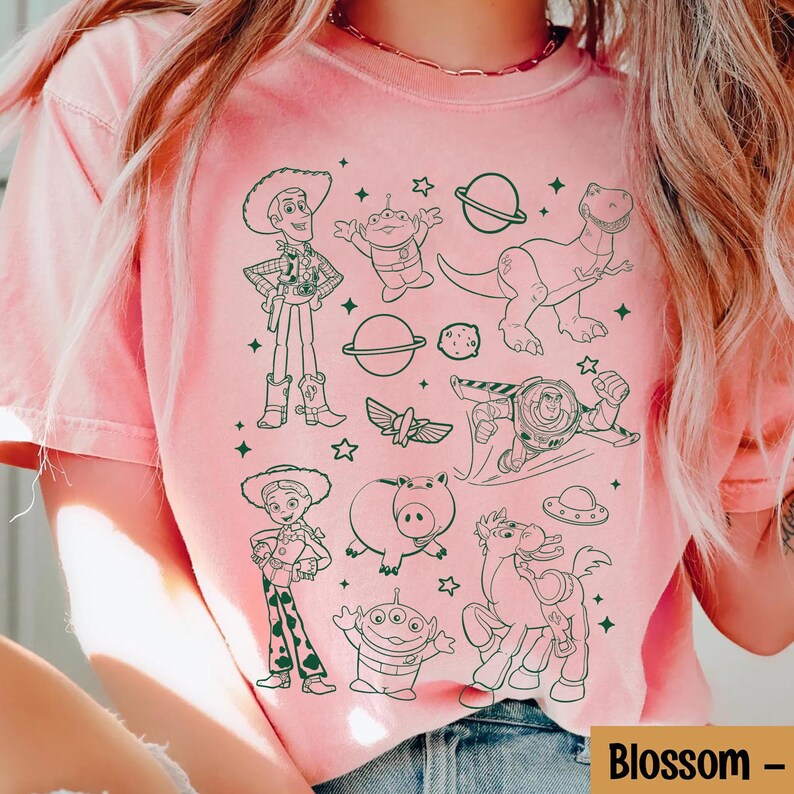 Puede incluir: Camiseta rosa claro con un dibujo lineal en blanco y negro de personajes de una pel&iacute;cula de animaci&oacute;n popular. La camiseta incluye el texto "Blossom -" en blanco.