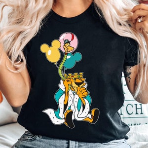 May include: Black t-shirt with a graphic of a cartoon lion wearing a crown and holding balloons. The balloons are pink, yellow, and blue. The lion is wearing a blue and white robe.