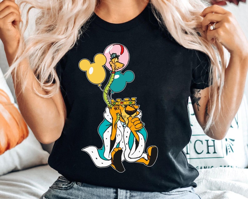 May include: Black t-shirt with a graphic of a cartoon lion wearing a crown and holding balloons. The balloons are pink, yellow, and blue. The lion is wearing a blue and white robe.