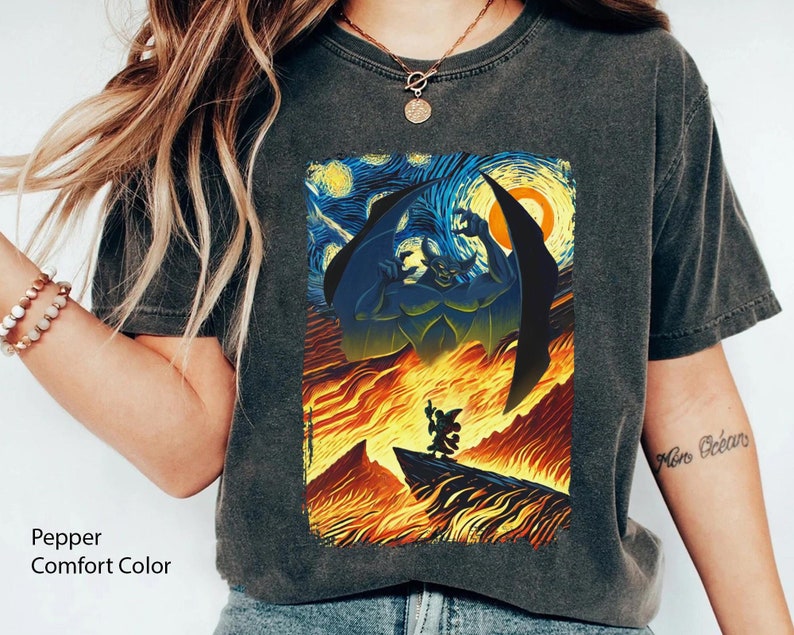 May include: A dark gray t-shirt with a vintage-style print of a cartoon character with wings, standing in front of a fiery background inspired by Vincent van Gogh's Starry Night. The text "More Ocean" is written on the right sleeve of the shirt.