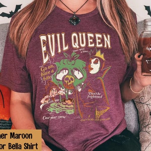 May include: Heather maroon t-shirt with a graphic print of the Evil Queen from Snow White. The graphic features the Evil Queen holding a poisoned apple and the text "Evil Queen", "Go on, have a bite", "Don't be frightened", "Cast your curse", and "Don't let the wind grow cold".