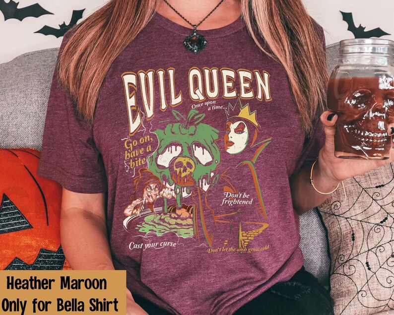 May include: Heather maroon t-shirt with a graphic print of the Evil Queen from Snow White. The graphic features the Evil Queen holding a poisoned apple and the text "Evil Queen", "Go on, have a bite", "Don't be frightened", "Cast your curse", and "Don't let the wind grow cold".