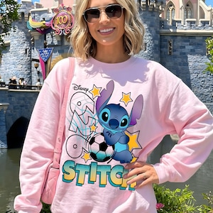 May include: Pink sweatshirt featuring a graphic of the Disney character Stitch with a soccer ball and the words "Run Go Stitch". The design includes yellow stars and a blue and yellow color scheme.
