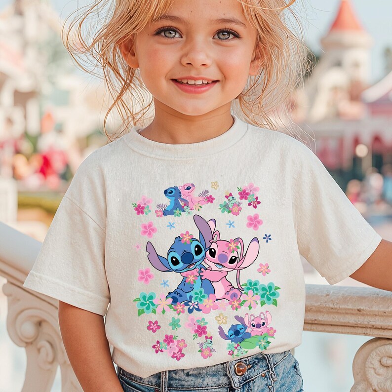 May include: Off-white t-shirt featuring a colorful graphic of the characters Stitch and Angel surrounded by flowers. The design includes Stitch in blue and Angel in pink, with floral accents in pink, green, and blue. The shirt is worn by a young girl.