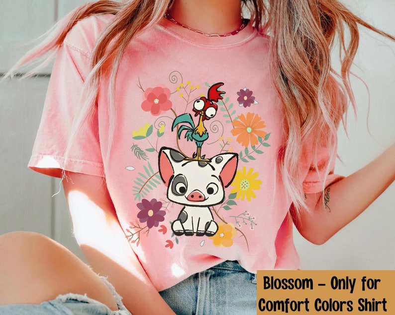 Pu&ograve; includere: Una maglietta rosa con un'immagine di un maiale e un gallo con fiori in stile cartone animato. Il testo "Blossom - Only for Comfort Colors Shirt" &egrave; in basso nell'immagine.