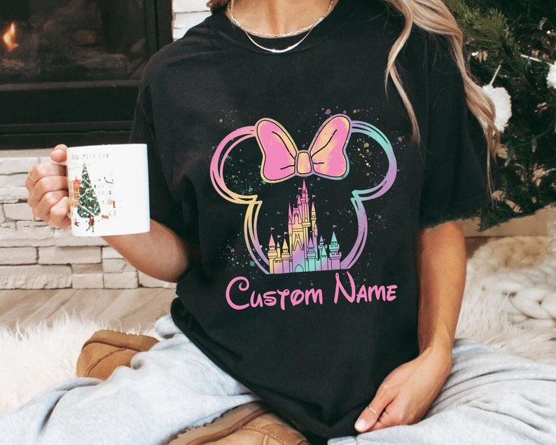 K&ouml;nnte beinhalten: Schwarzes T-Shirt mit einem farbenfrohen Minnie-Mouse-Design, einschlie&szlig;lich Schleife, Schloss und dem Text "Custom Name". Das Design verwendet Pastellfarben und einen Spritzeffekt. Dies ist ein Freizeitkleidungsst&uuml;ck.