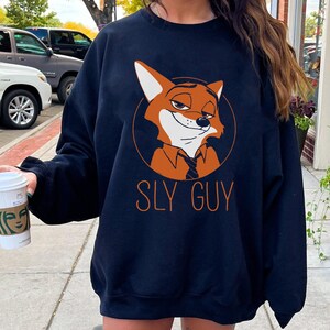 May include: Navy blue sweatshirt with an orange cartoon fox wearing a tie, inside a circle. The text "SLY GUY" is printed below the fox in orange. The sweatshirt is a casual style, suitable for everyday wear.