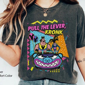 Puede incluir: Una camiseta negra con un gr&aacute;fico de estilo vintage de los 90 que presenta personajes de la serie animada "Las locuras del emperador". El gr&aacute;fico incluye el texto "Pull the Lever, Kronk" y presenta a Kronk, Yzma y Kuzco.