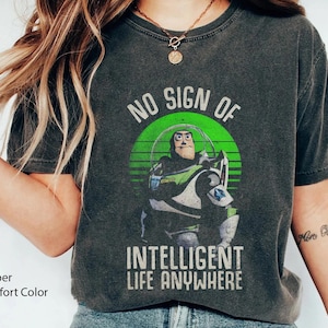 以下が含まれることがあります： トイストーリーの バズ・ライトイヤーの緑と白のグラフィックが特徴の、くすんだダークグレーのTシャツ。グラフィックには「No Sign of Intelligent Life Anywhere」というテキストが含まれています。