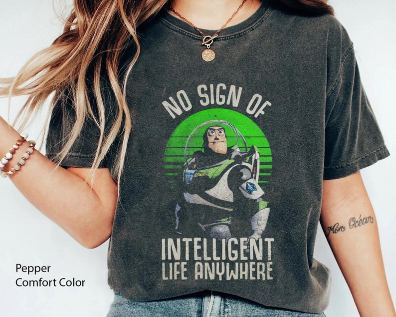 以下が含まれることがあります： トイストーリーの バズ・ライトイヤーの緑と白のグラフィックが特徴の、くすんだダークグレーのTシャツ。グラフィックには「No Sign of Intelligent Life Anywhere」というテキストが含まれています。