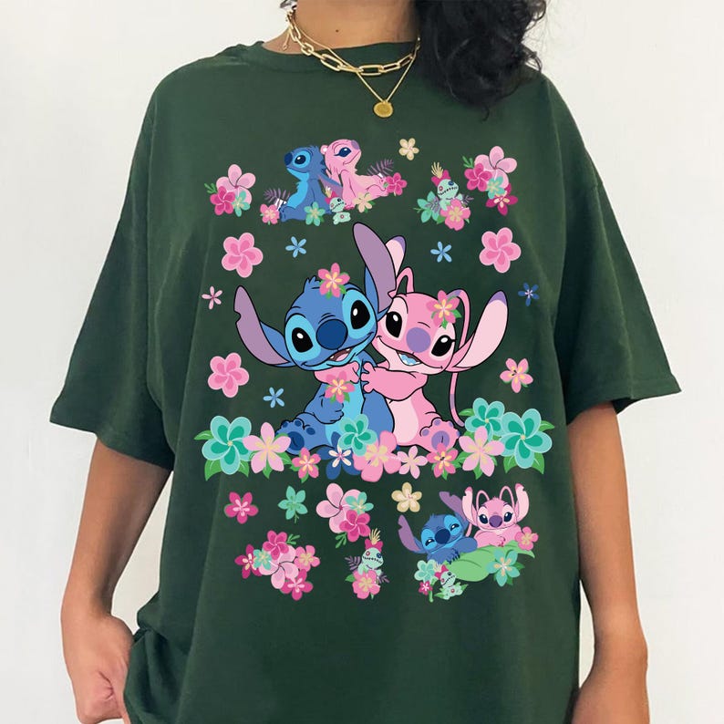 May include: Dark green t-shirt featuring a colorful graphic of the Disney characters Stitch and Angel, surrounded by pink and blue flowers. The design includes multiple images of the characters in various poses. The shirt is a casual, oversized style.