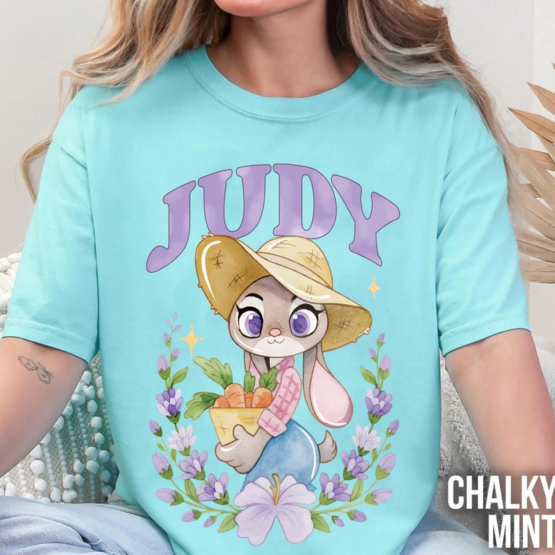 May include: A pale turquoise t-shirt with a cartoon bunny character named Judy, wearing a straw hat and holding a basket of carrots. The word "JUDY" is arched above the character in purple. Floral elements surround the character. The text "CHALKY MINT" is at the bottom right.
