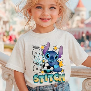 May include: A light beige t-shirt featuring the Disney character Stitch, holding a soccer ball. The shirt has the word "Stitch" in a gradient font, with stars and the Disney logo. The shirt is worn by a young child.
