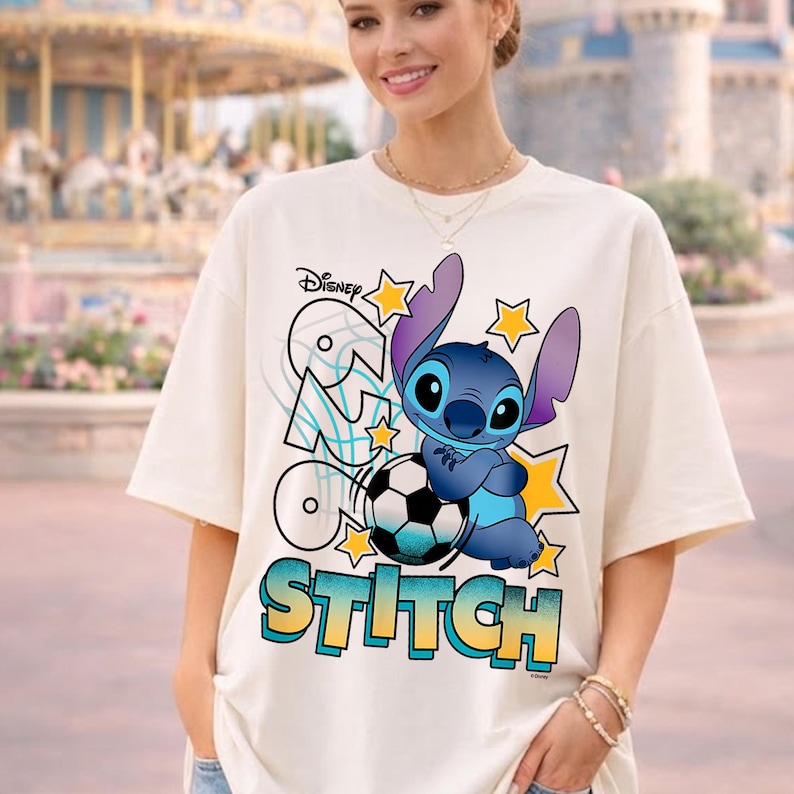 May include: Cream-colored t-shirt featuring a Disney Stitch graphic. The design includes Stitch, a soccer ball, stars, and the word "Stitch" in a colorful font. The Disney logo is also visible.