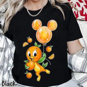 Puede incluir: Camiseta negra con un pájaro naranja de dibujos animados sosteniendo una naranja y un globo con forma de Mickey Mouse. El pájaro tiene hojas verdes como alas y está rodeado de naranjas y rodajas de naranja. La palabra "Black" está impresa en la parte inferior.