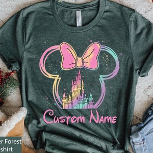 K&ouml;nnte beinhalten: Heather Forest Green Bella T-Shirt mit einem farbenfrohen Minnie Mouse-Design. Das Design umfasst eine rosa Schleife, ein Schloss und die Worte "Custom Name" in Pink. Das Design ist in Regenbogenfarben umrandet.