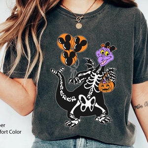 May include: A charcoal grey short-sleeve t-shirt featuring a graphic of a purple dragon wearing a skeleton costume, holding three orange balloons with black Mickey Mouse silhouettes and an orange jack-o'-lantern candy bucket.