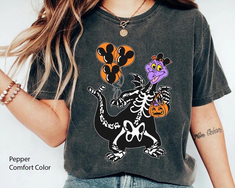 May include: A charcoal grey short-sleeve t-shirt featuring a graphic of a purple dragon wearing a skeleton costume, holding three orange balloons with black Mickey Mouse silhouettes and an orange jack-o'-lantern candy bucket.