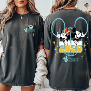 May include: Dark grey t-shirt with Mickey and Minnie Mouse graphics, the text "2020", and "Disney Vacation Club MEMBER". The front has a small Mickey and Minnie graphic. The back features a larger design.