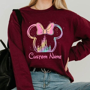 K&ouml;nnte beinhalten: Burgunderfarbenes Sweatshirt mit einem Minnie Mouse-Design, Schloss und Schleifen-Grafik. Das Design enth&auml;lt den Text "Custom Name" in Rosa. Das Sweatshirt hat eine einfarbige Burgunderfarbe.