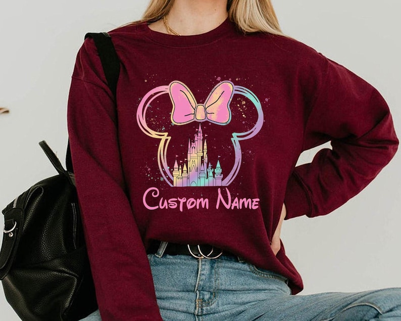 K&ouml;nnte beinhalten: Burgunderfarbenes Sweatshirt mit einem Minnie Mouse-Design, Schloss und Schleifen-Grafik. Das Design enth&auml;lt den Text "Custom Name" in Rosa. Das Sweatshirt hat eine einfarbige Burgunderfarbe.
