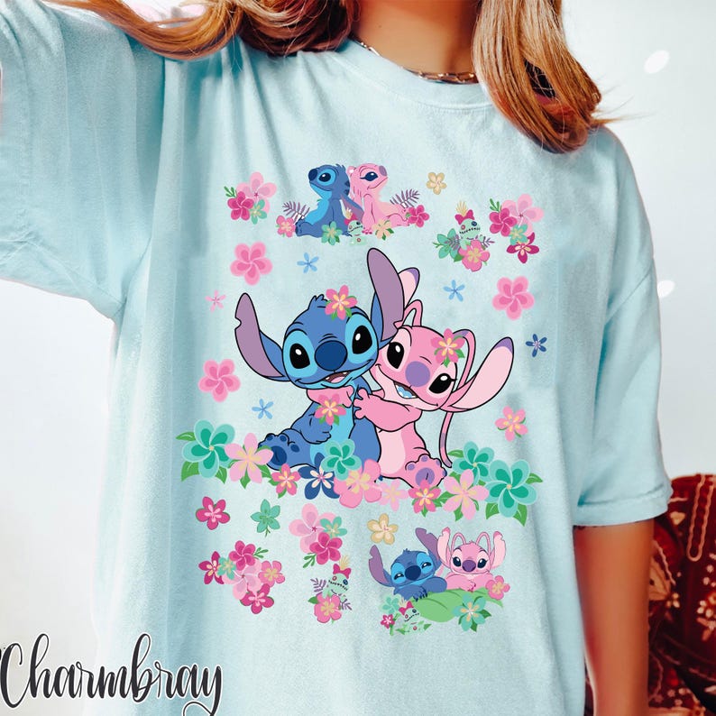 May include: Light blue t-shirt featuring a graphic of Stitch and Angel surrounded by pink and purple flowers. The design includes multiple images of the characters. The word "Charmbray" is printed in a cursive font at the bottom left.