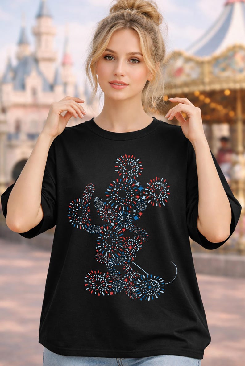 May include: Black t-shirt featuring a colorful firework design in the shape of a famous cartoon character. The design incorporates red, white, and blue elements. The shirt is a crew neck style.
