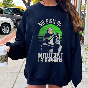 以下が含まれることがあります： トイストーリーの バズ・ライトイヤーが描かれた、緑、白、青のグラフィックが施された黒いスウェットシャツ。グラフィックには「No Sign of Intelligent Life Anywhere」というテキストが含まれています。