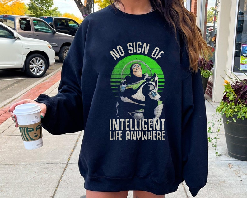 以下が含まれることがあります： トイストーリーの バズ・ライトイヤーが描かれた、緑、白、青のグラフィックが施された黒いスウェットシャツ。グラフィックには「No Sign of Intelligent Life Anywhere」というテキストが含まれています。