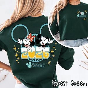 May include: A forest green sweatshirt with a design featuring Mickey and Minnie Mouse, the year 2026, and the text "Disney Vacation Club MEMBER". The design includes a Mickey Mouse ear outline and stars.