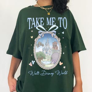 May include: Dark green t-shirt with the text "TAKE ME TO Walt Disney World" in light blue script. The shirt features a framed image of a Disney park with a castle, tower, and sphere. Mickey Mouse icons are on the shirt.