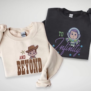 Puede incluir: Dos sudaderas con dise&ntilde;os de personajes de dibujos animados. Una es de color crema con un gr&aacute;fico de vaquero y las palabras "AND BEYOND" en marr&oacute;n. La otra es gris oscuro con un gr&aacute;fico de Buzz Lightyear y las palabras "TO Infinity" en morado.