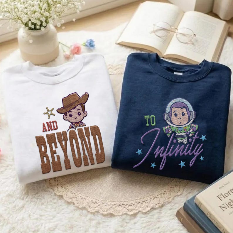 Puede incluir: Dos sudaderas bordadas, una blanca y otra azul marino. La sudadera blanca presenta un vaquero y el texto "AND BEYOND". La sudadera azul marino tiene un astronauta y el texto "TO Infinity".