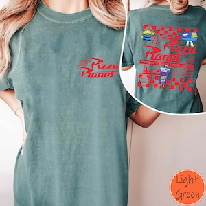 Op de afbeelding: Een lichtgroen T-shirt met een rode afbeelding van het Pizza Planet-logo. De achterkant van het shirt heeft een rood-wit geruit ontwerp met een Pizza Planet-logo, een cartoon-alien en een pizzadoos.