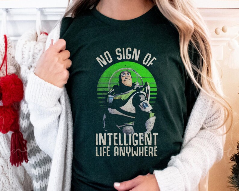 以下が含まれることがあります： トイストーリーの Buzz Lightyear のレトロなグラフィックがプリントされた緑色の T シャツ。グラフィックには「No sign of intelligent life anywhere」というテキストが含まれています。