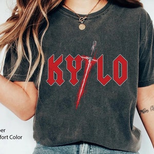 May include: A dark grey t-shirt with a red graphic of the word "KYLO" in a heavy metal font with a red lightsaber behind it.