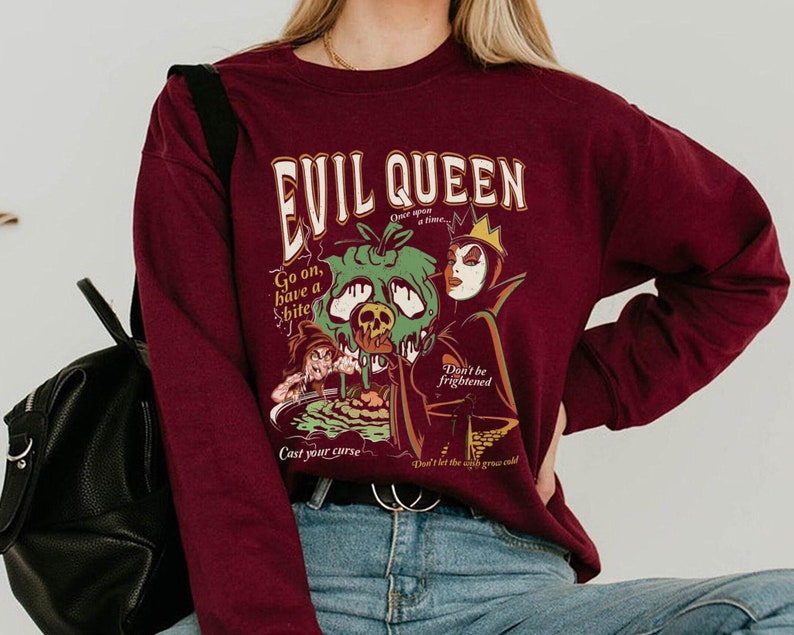 May include: Burgundy sweatshirt with a graphic print of the Evil Queen from Snow White. The graphic features the Evil Queen holding a poisoned apple and the text "Evil Queen, Once upon a time, Go on, have a bite! Don't be frightened, Don't let the witch grow cold, Cast your curse".