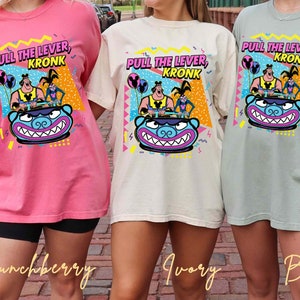 Puede incluir: Tres camisetas con un estampado gr&aacute;fico de un personaje de dibujos animados de la serie animada 'Las locuras del emperador'. El personaje est&aacute; montando un paseo con el texto 'Tira de la palanca, Kronk' en las camisetas.