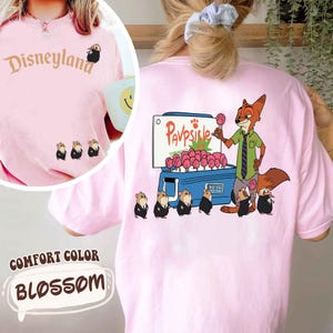 Puede incluir: Camiseta rosa Comfort Color con un gr&aacute;fico de Disneyland en la parte delantera y una imagen de dibujos animados de Nick Wilde vendiendo paletas en la parte trasera. La camiseta tambi&eacute;n presenta un grupo de peque&ntilde;os personajes animales. La palabra "BLOSSOM" est&aacute; impresa en la parte inferior.
