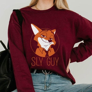 May include: Burgundy sweatshirt with a cartoon fox character in a circular design. The fox has a sly expression, and the text "SLY GUY" is printed below. The sweatshirt is a solid colour and has long sleeves.