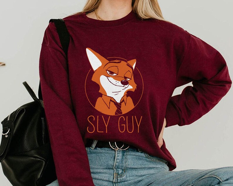 May include: Burgundy sweatshirt with a cartoon fox character in a circular design. The fox has a sly expression, and the text "SLY GUY" is printed below. The sweatshirt is a solid colour and has long sleeves.