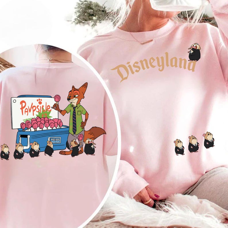 Puede incluir: Sudadera rosa claro con un zorro de dibujos animados vendiendo paletas de un refrigerador azul, con la palabra "Pavpsicle". La palabra "Disneyland" est&aacute; impresa en oro en la parte delantera, con personajes de dibujos animados.