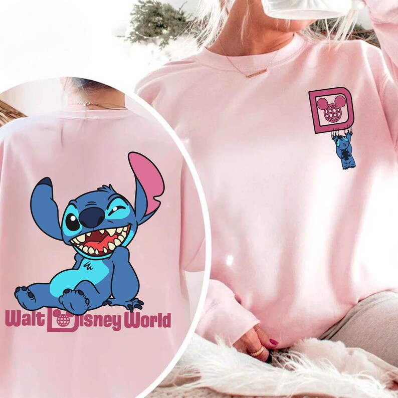May include: A light pink sweatshirt featuring a cartoon Stitch design. The front has a small Stitch graphic hanging from a pink square with a Mickey Mouse head. The back displays a larger Stitch graphic with the text "Walt Disney World".