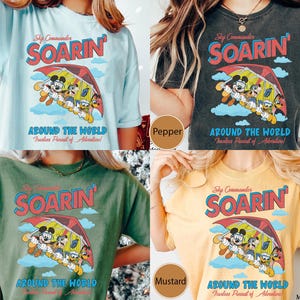 Puede incluir: Cuatro camisetas de diferentes colores con un gr&aacute;fico de estilo vintage de Mickey Mouse y sus amigos volando en un ala delta. El gr&aacute;fico incluye el texto "Sky Commander Soarin' Around the World Fearless Pursuit of Adventure!"