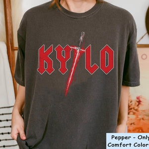 May include: A dark grey t-shirt with a red graphic of a lightsaber and the word "KYLO" in red letters. The shirt is a comfort colour shirt.