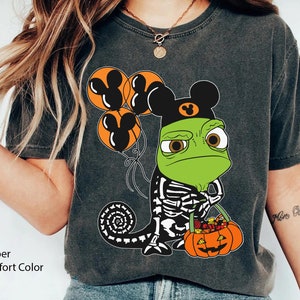 May include: A charcoal grey t-shirt featuring a graphic of a green chameleon wearing a black skeleton costume and a black mouse-ear hat. The chameleon holds a pumpkin-shaped bucket filled with sweets and three orange mouse-ear balloons.
