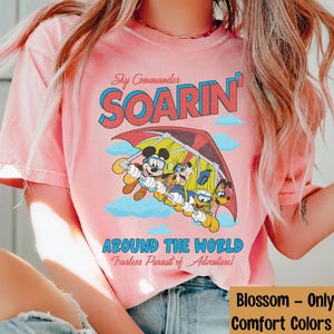 Puede incluir: Camiseta rosa con un gr&aacute;fico de Mickey Mouse y sus amigos volando en un ala delta. El texto "Sky Commander SOARIN' AROUND THE WORLD Fearless Pursuit of Adventure!" est&aacute; impreso en la camiseta.