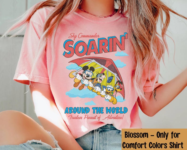Puede incluir: Camiseta rosa con un gr&aacute;fico de Mickey Mouse y sus amigos volando en un ala delta. El texto "Sky Commander SOARIN' AROUND THE WORLD Fearless Pursuit of Adventure!" est&aacute; impreso en la camiseta.